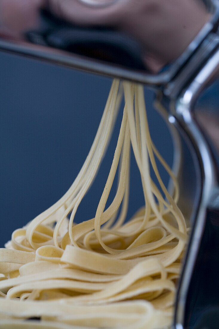 Haufen frischer Tagliatelle, die aus einer Nudelmaschine kommen