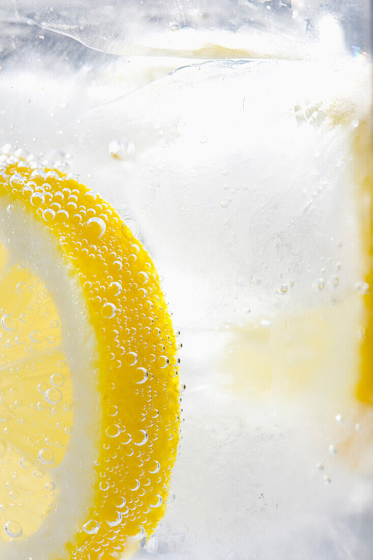 Extreme Nahaufnahme einer Zitronenscheibe, die in sprudelndem Eiswasser schwimmt
