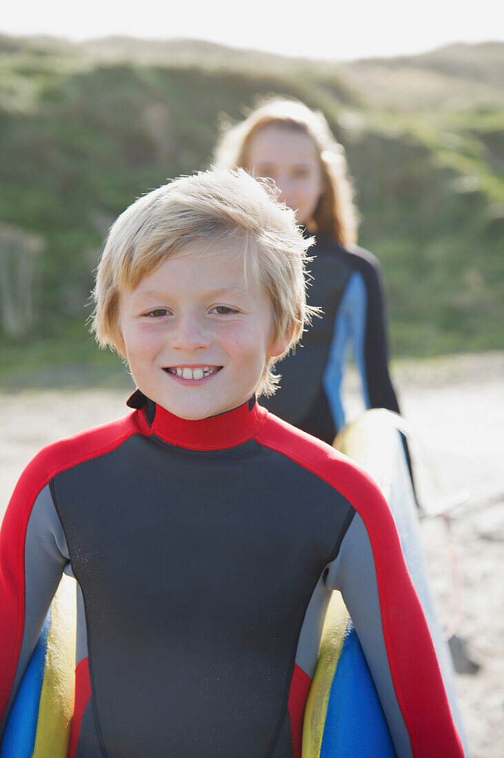 Lächelnder Junge in einem Neoprenanzug, der ein Surfbrett mit einem Mädchen trägt