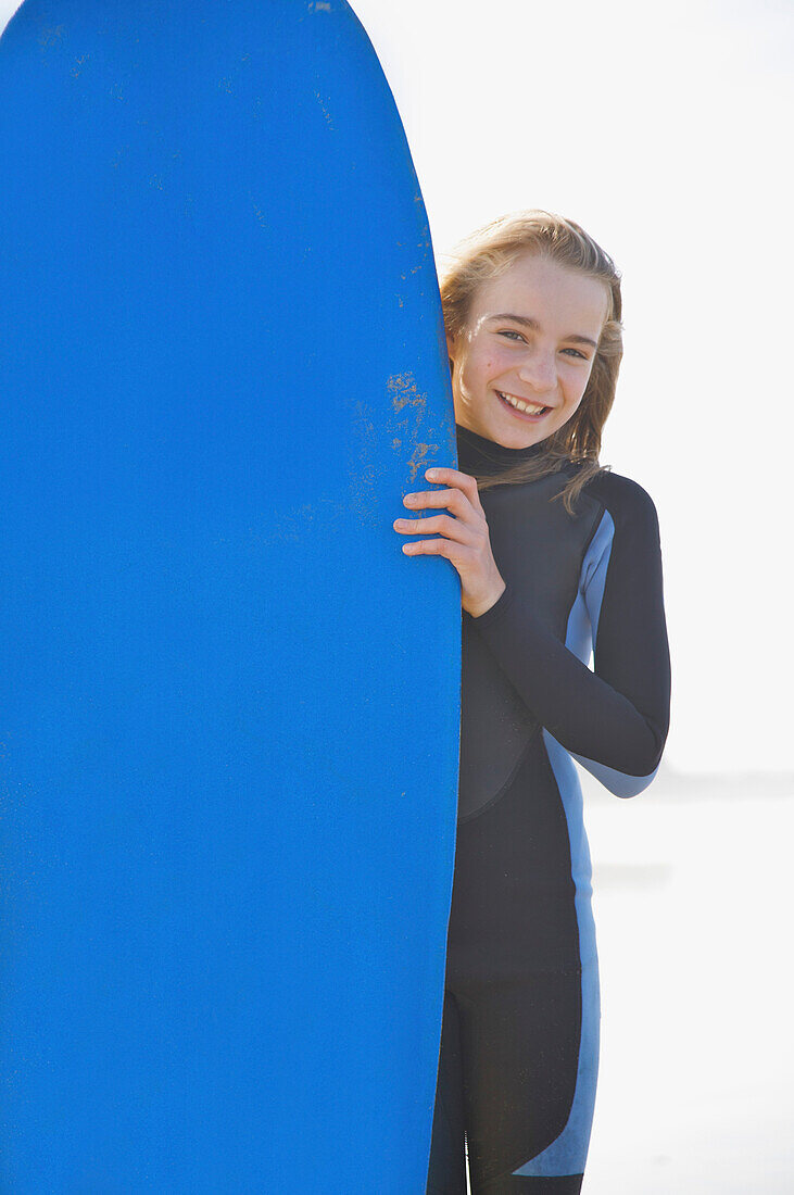 Lächelndes Mädchen, das ein Surfbrett aufrecht hält