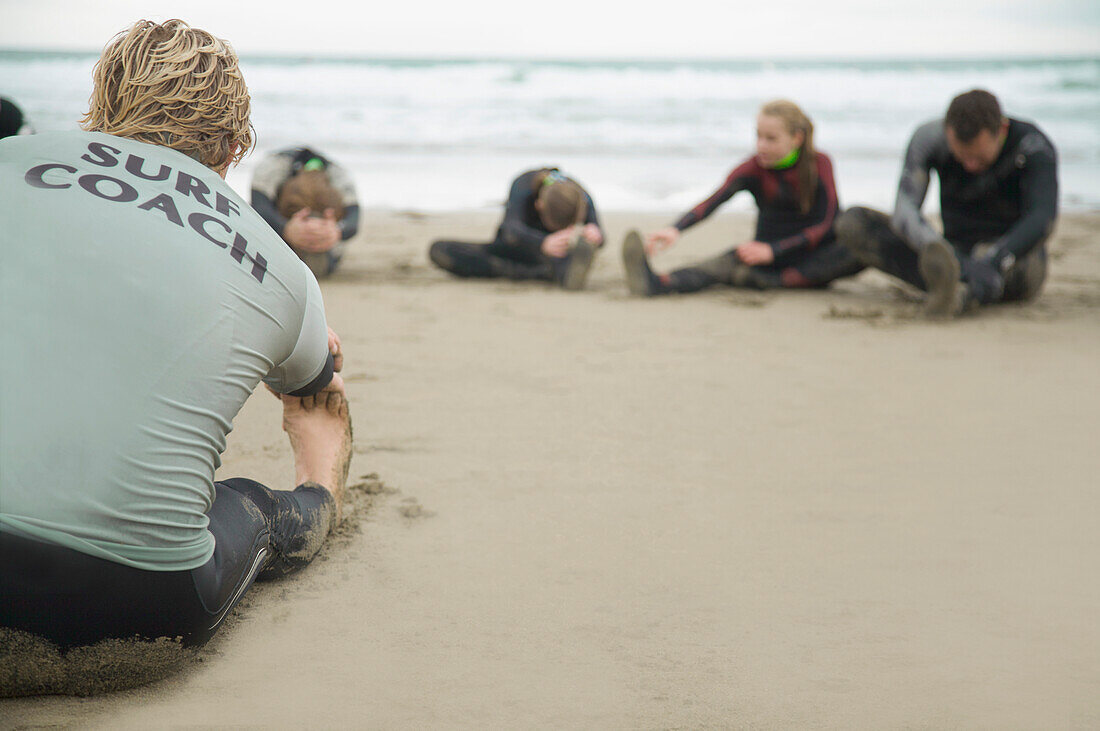 Rückenansicht eines Surflehrers und einer Gruppe von Schülern, die sich am Strand die Beine vertreten