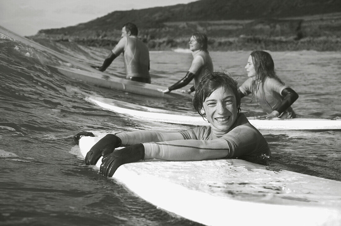 Lächelnder Jugendlicher im Meer, der sich an seinem Surfbrett festhält