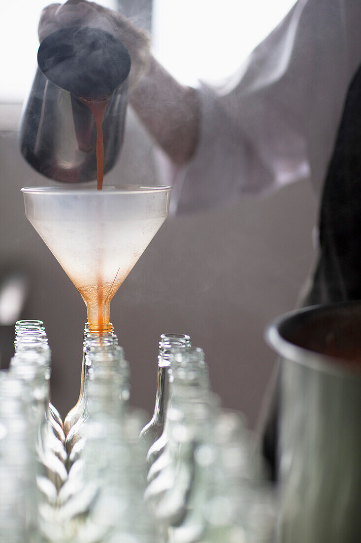 Factory worker pouring tomato sauce through a funnel into bottles - headless