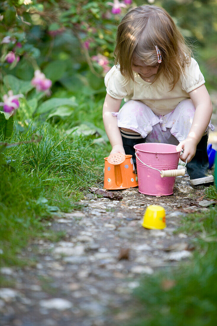 Junges Mädchen hockt in einem Garten und spielt mit Gartenspielzeug