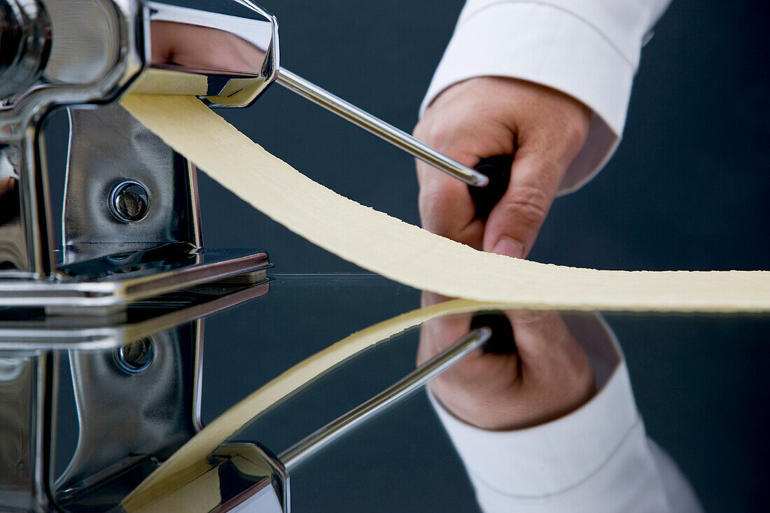 Close up of a chef hand turning the handle of a pasta maker with pasta dough coming out
