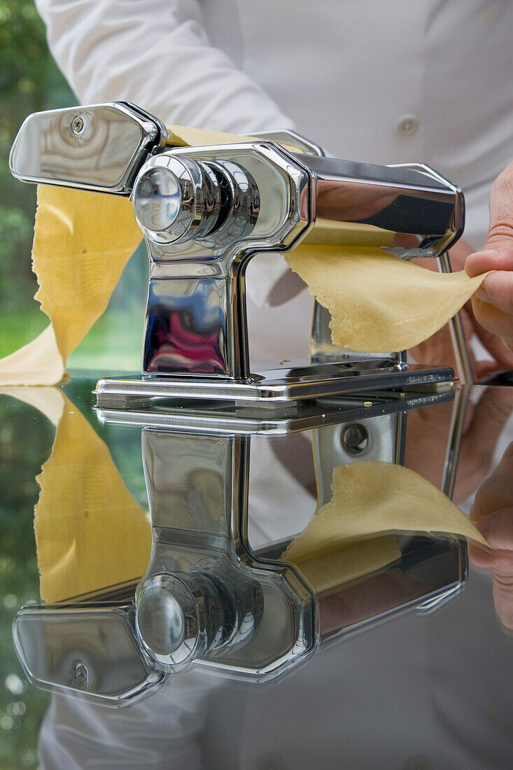 Chef stretching pasta dough out of a pasta maker