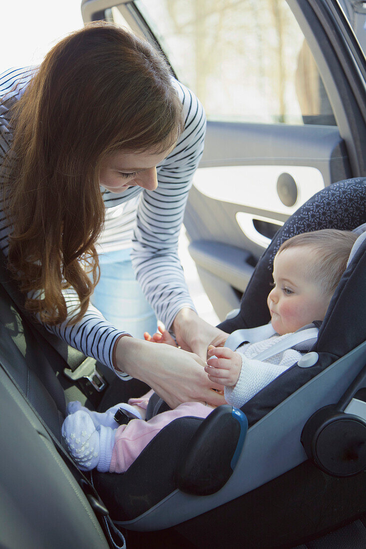 Woman Fastening Baby Girl Safety Seat in Car