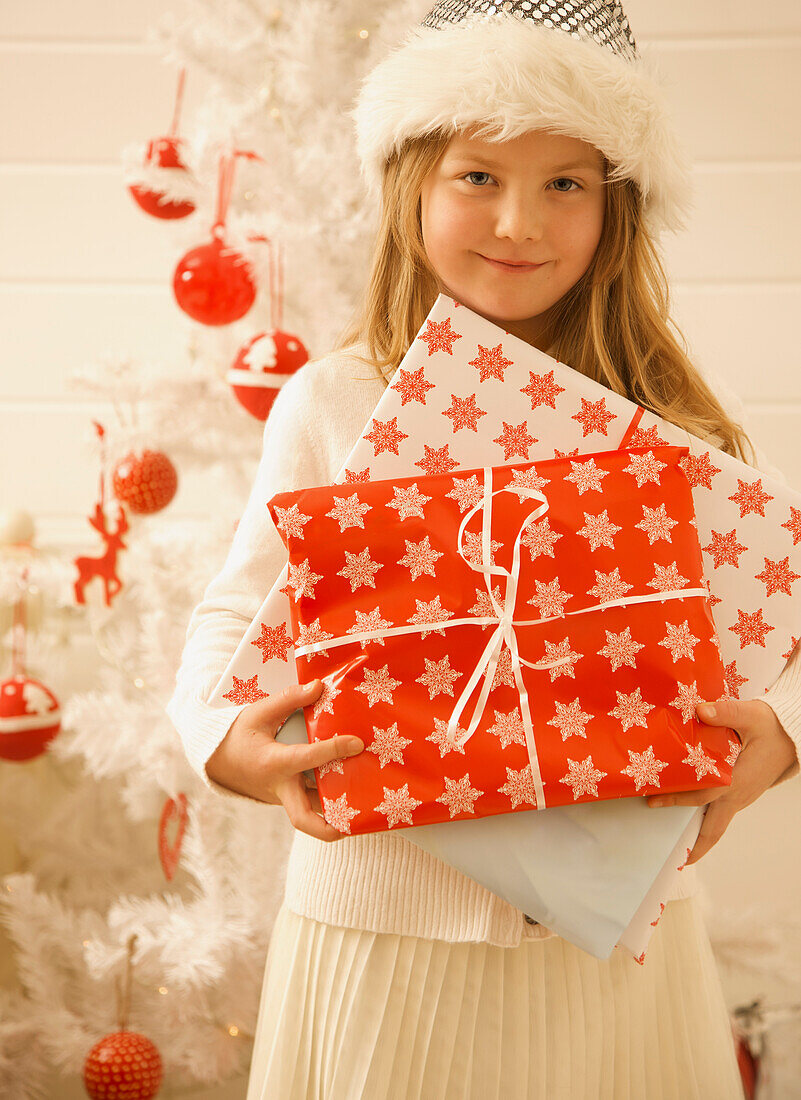 Mädchen steht an einem Weihnachtsbaum und hält Geschenke