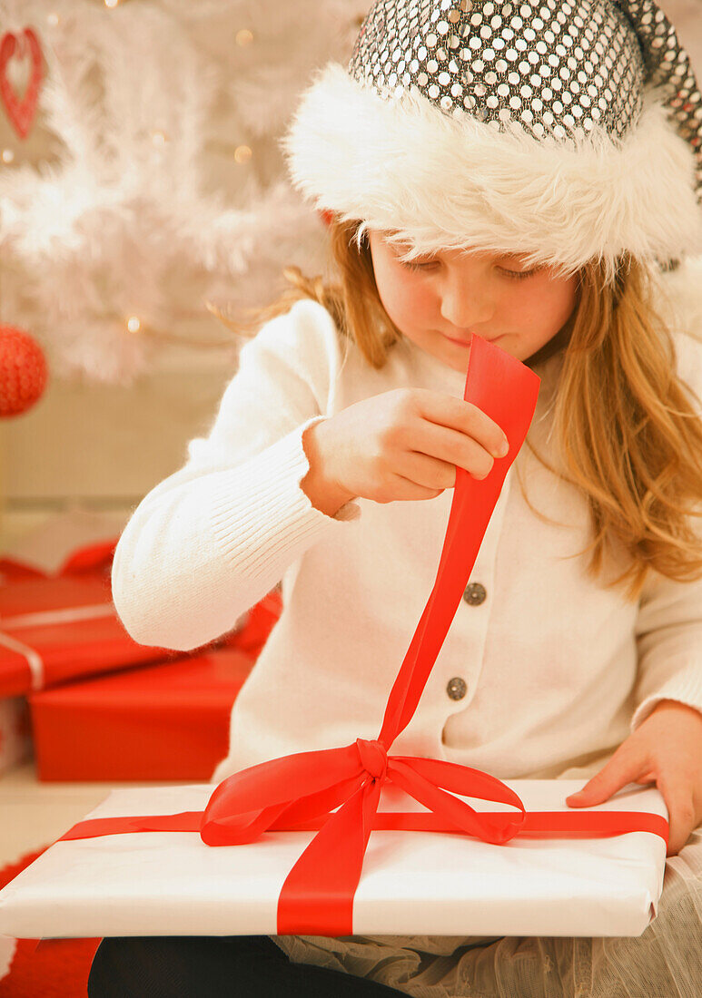 Mädchen mit einer Pelzmütze packt ein Weihnachtsgeschenk aus