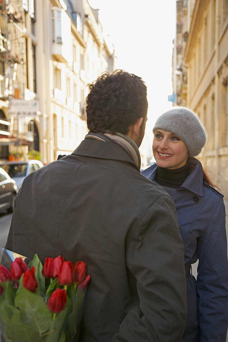 Back view of a man holding flowers behind his back standing in front of a woman