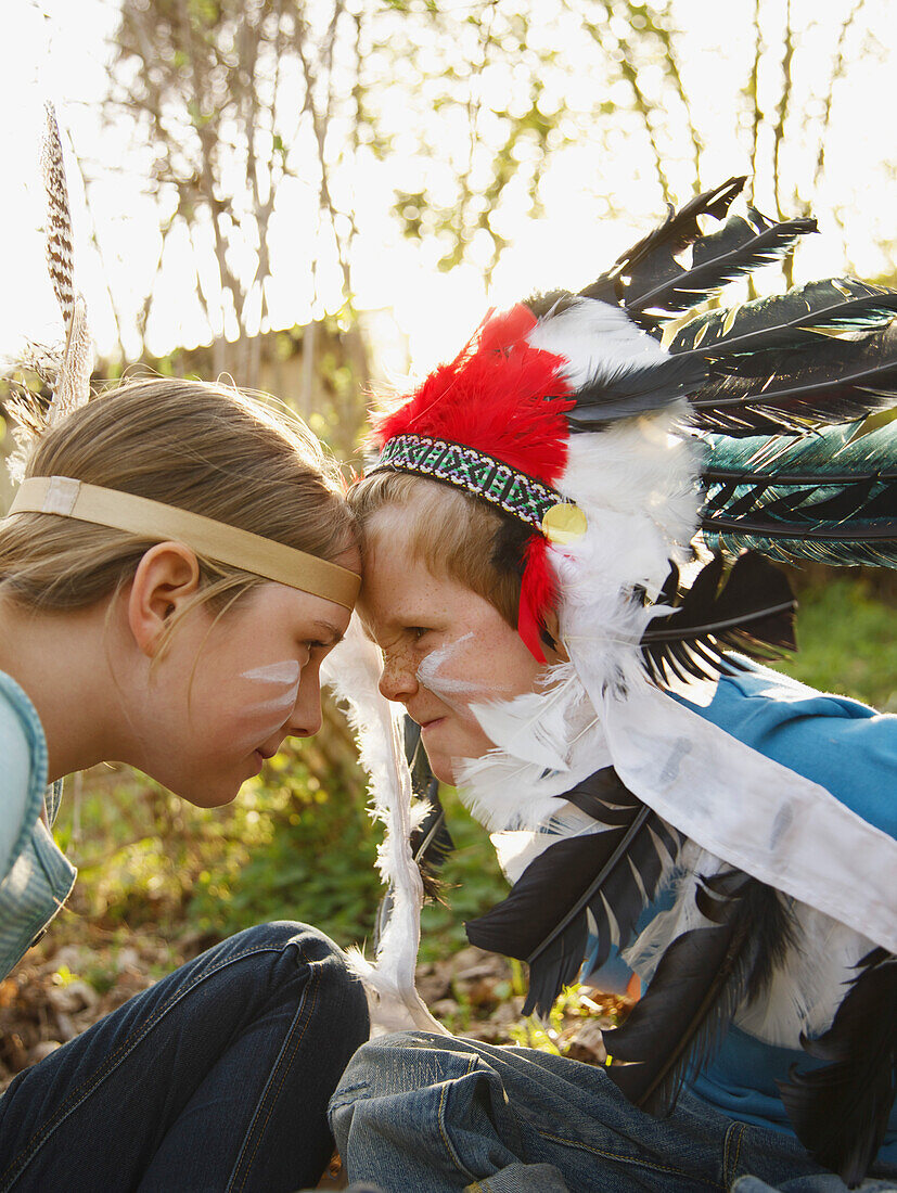Junge und Mädchen mit indianischem Federkopfschmuck sitzen sich Auge in Auge gegenüber