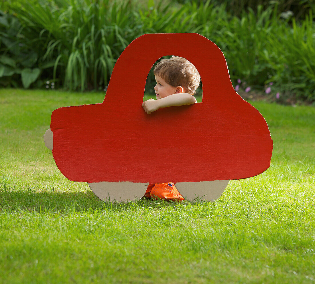 Young Boy Kneeling behind Cardboard Cut Out in Shape of Car