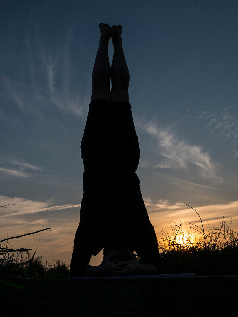Mann übt Yoga im Freien bei Sonnenuntergang, Kopfstand-Pose