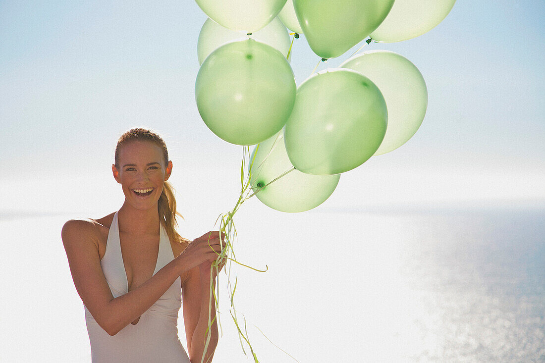 Nahaufnahme einer Frau, die ein Bündel grüner Luftballons hält und lächelt