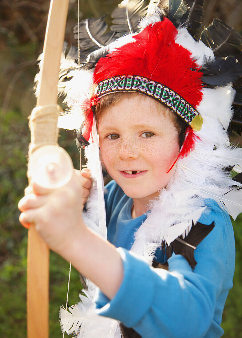 Boy wearing indian chief feather headdress holding bow and arrow
