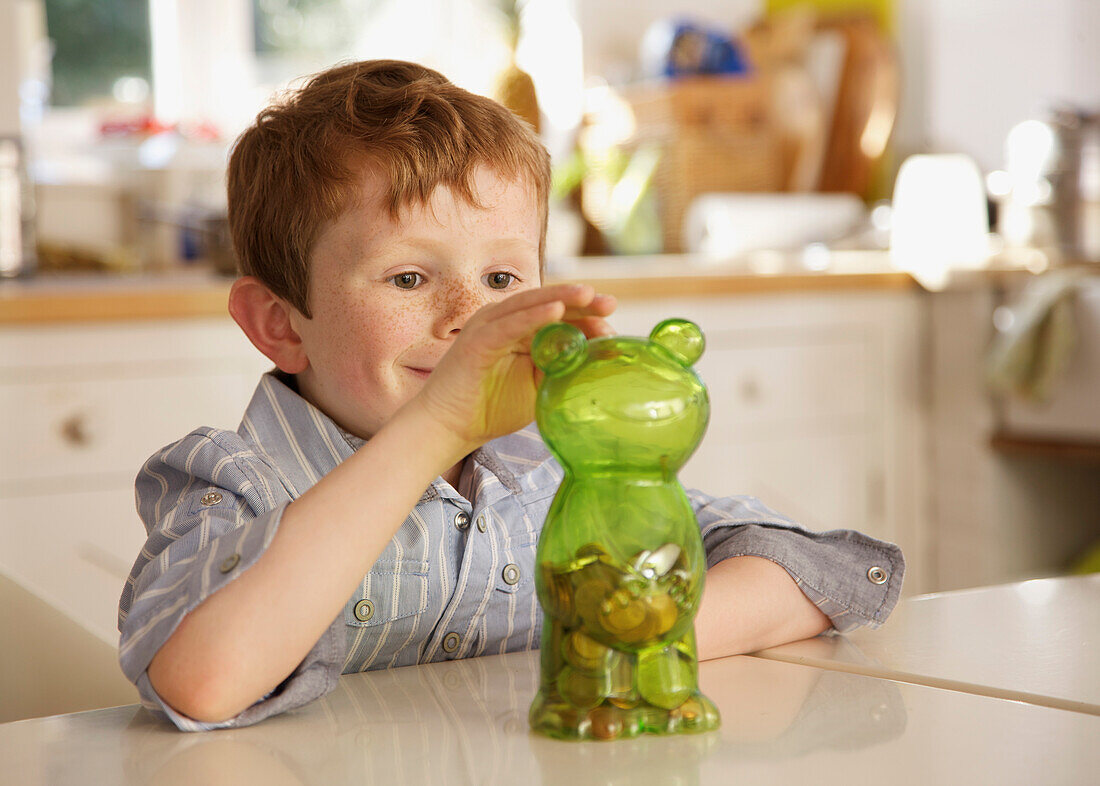 Boy putting coins into a money box in the shape of a teddy bear