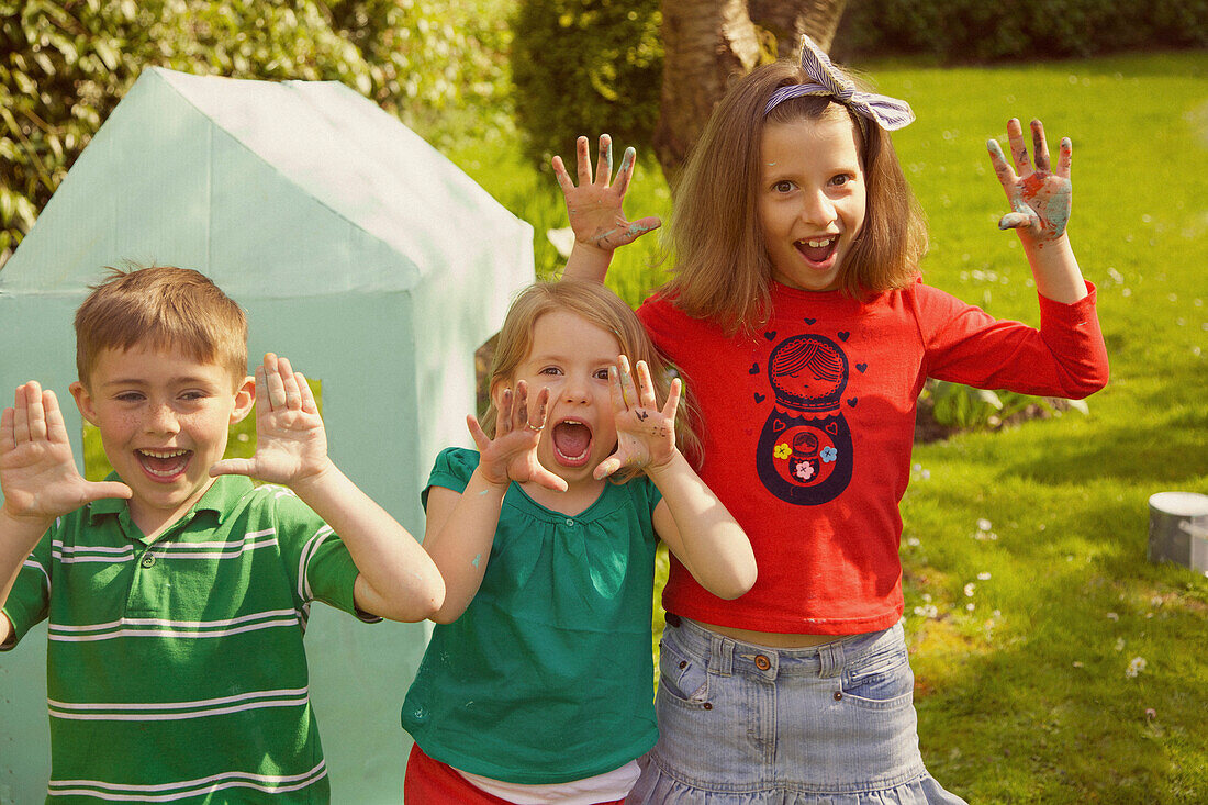 Smiling Children with Hands Raised in Garden