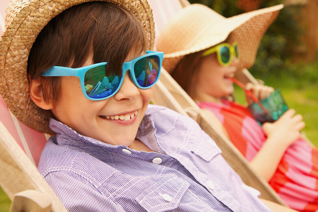 Junge und Mädchen mit Strohhut und Sonnenbrille, lächelnd
