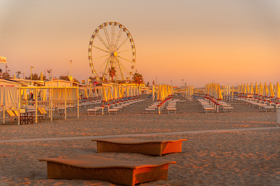 Blick auf Riesenrad und Sonnenschirme auf dem Lido am Strand von Rimini bei Sonnenaufgang, Rimini, Emilia-Romagna, Italien, Europa