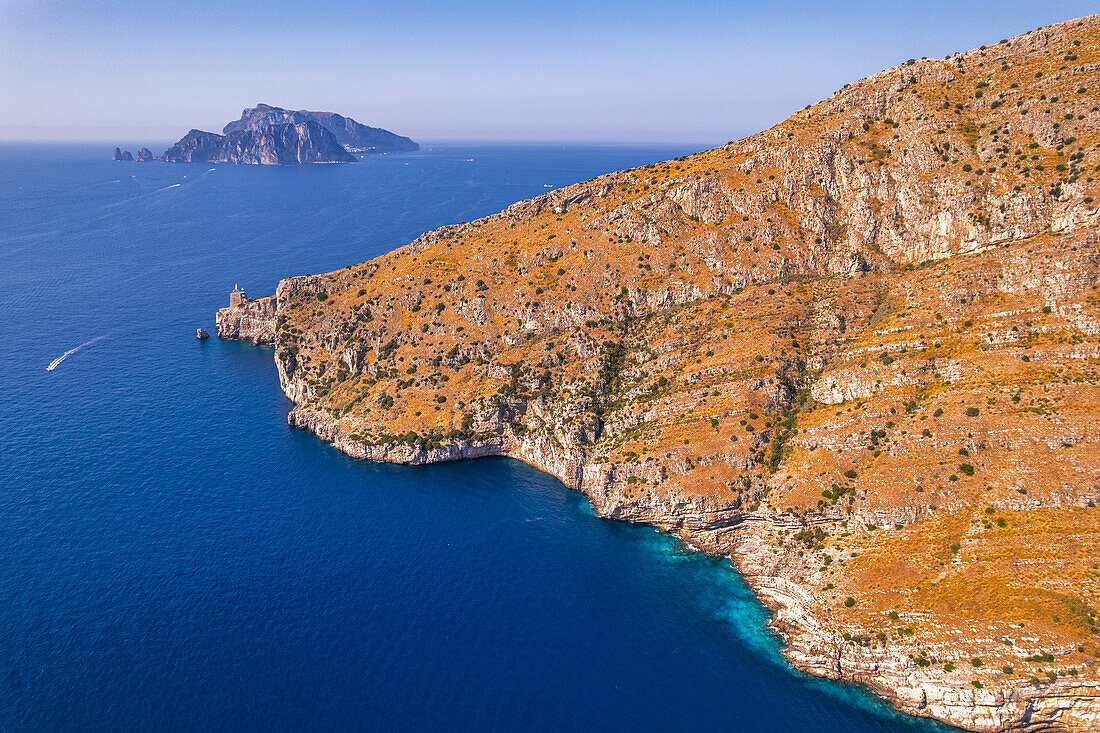 Luftaufnahme einer Felsenküste vor dem blauen Wasser des Tyrrhenischen Meeres mit der Insel Capri im Hintergrund, Amalfiküste, Provinz Neapel, Region Kampanien, Süditalien, Italien, Europa
