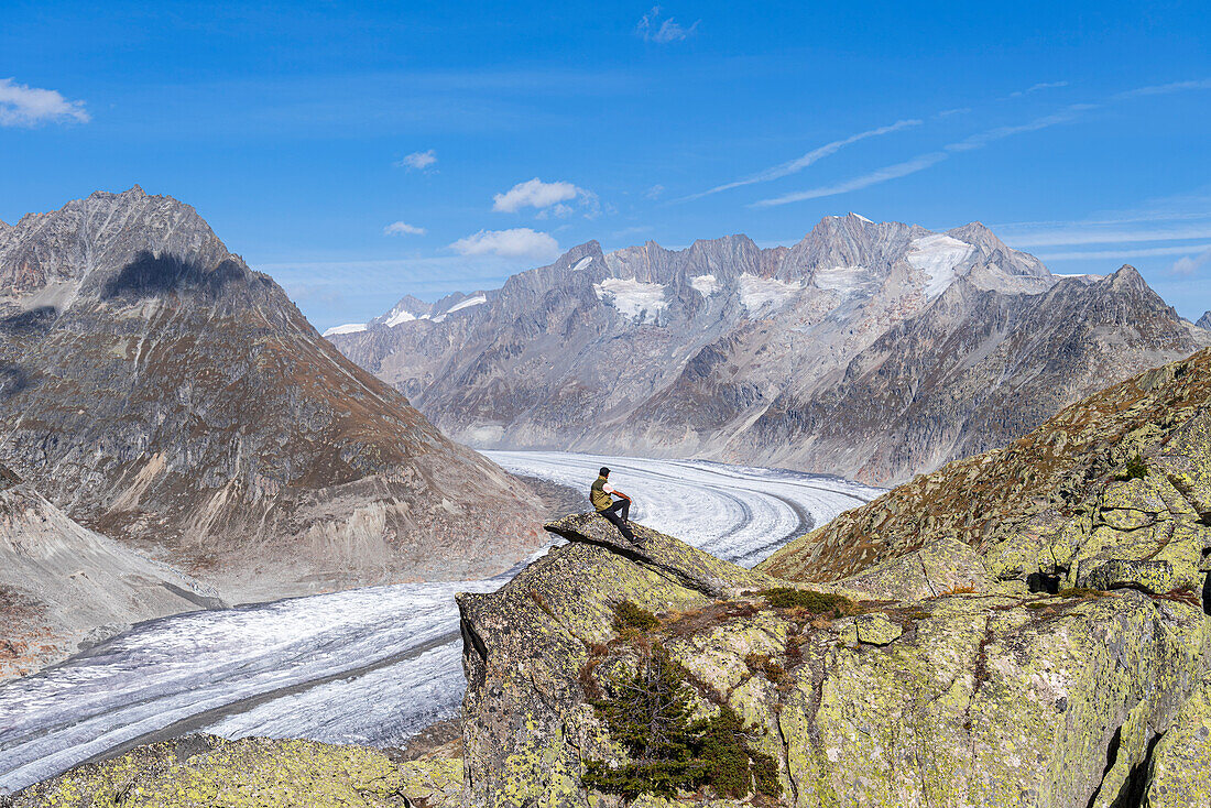 Wanderer auf einem Felsen, der die Aussicht auf den Aletschgletscher und die verschneiten Alpen genießt, Aletschgletscher, Bettmerhorn, UNESCO-Welterbe, Kanton Wallis, Schweiz, Europa