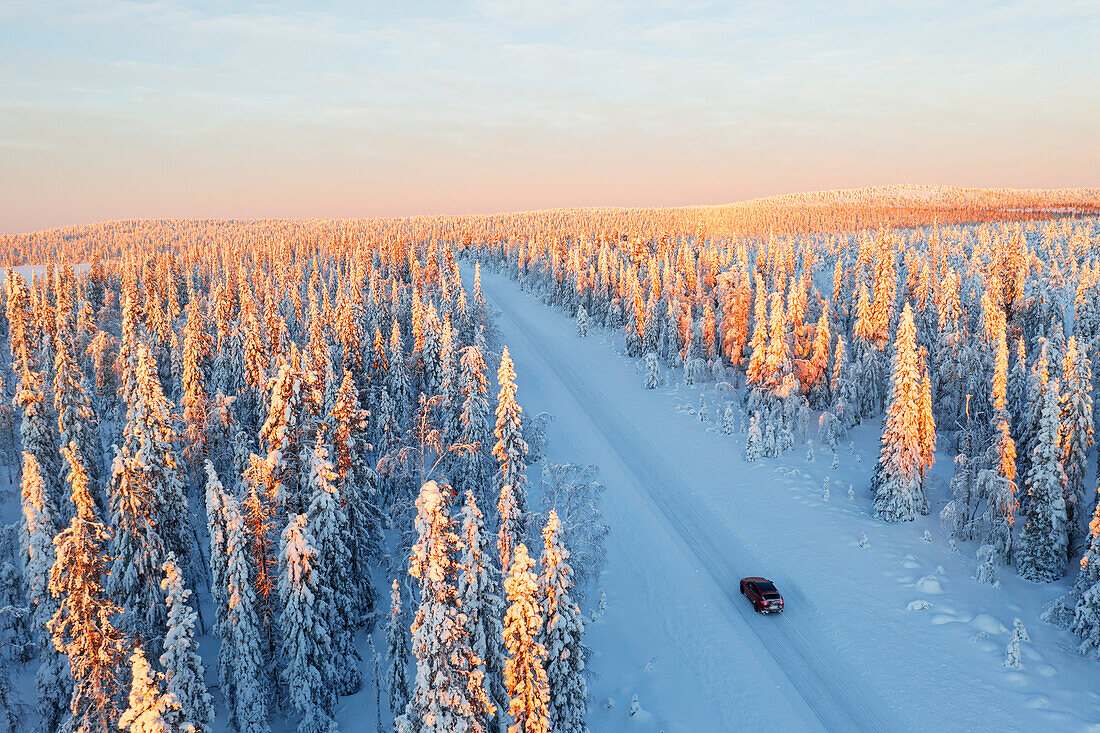 Blick aus einer Drohne auf ein Auto auf einer vereisten Straße in einem Kiefernwald bei Sonnenaufgang, Schwedisch Lappland, Schweden, Skandinavien, Europa