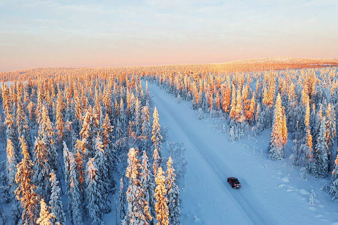 View from a drone of a car travelling an icy road among pine tree wood at sunrise, Swedish Lapland, Sweden, Scandinavia, Europe