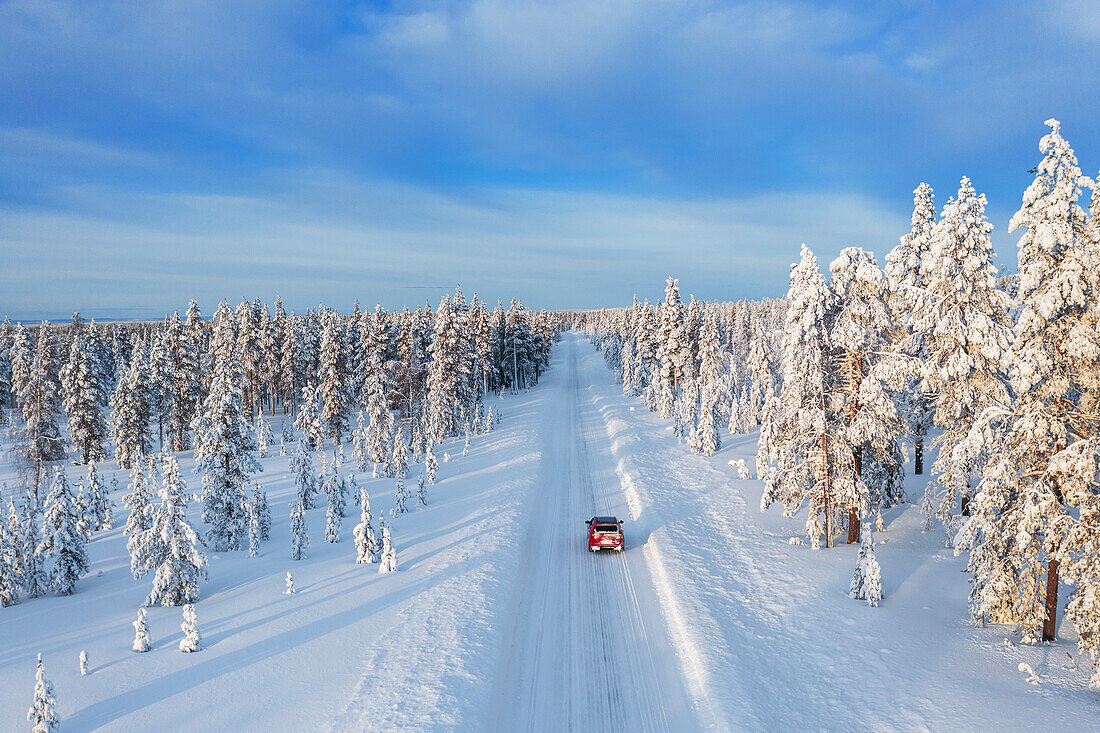 Drohnenansicht eines Autos auf einer leeren und gefrorenen Straße in der weißen Landschaft von Schwedisch-Lappland, Schweden, Skandinavien, Europa