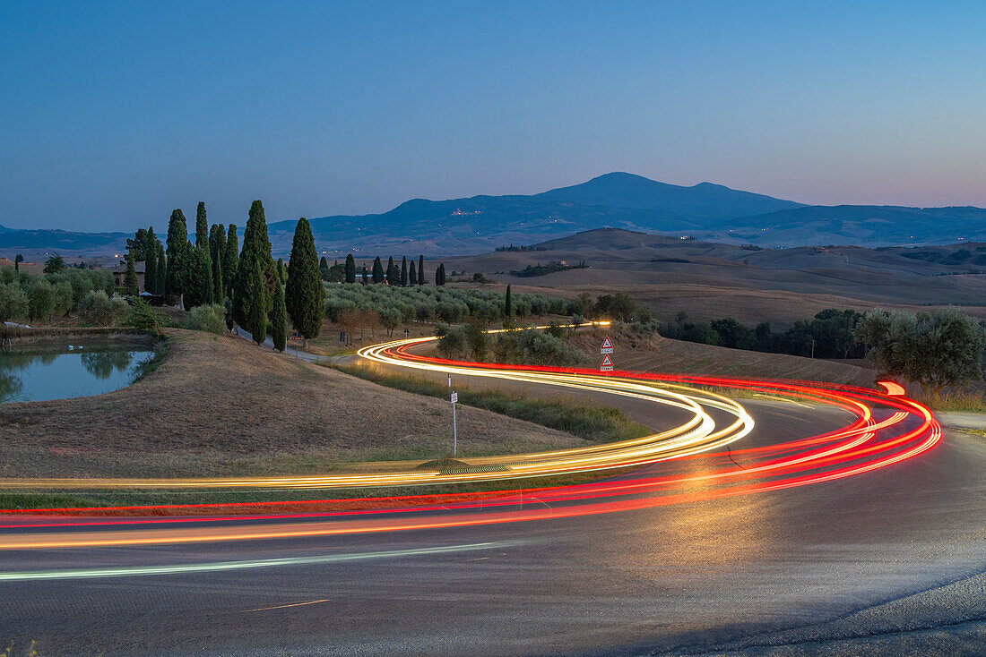 Blick auf Autolichter in der toskanischen Landschaft bei Pienza in der Abenddämmerung, Pienza, Provinz Siena, Toskana, Italien, Europa