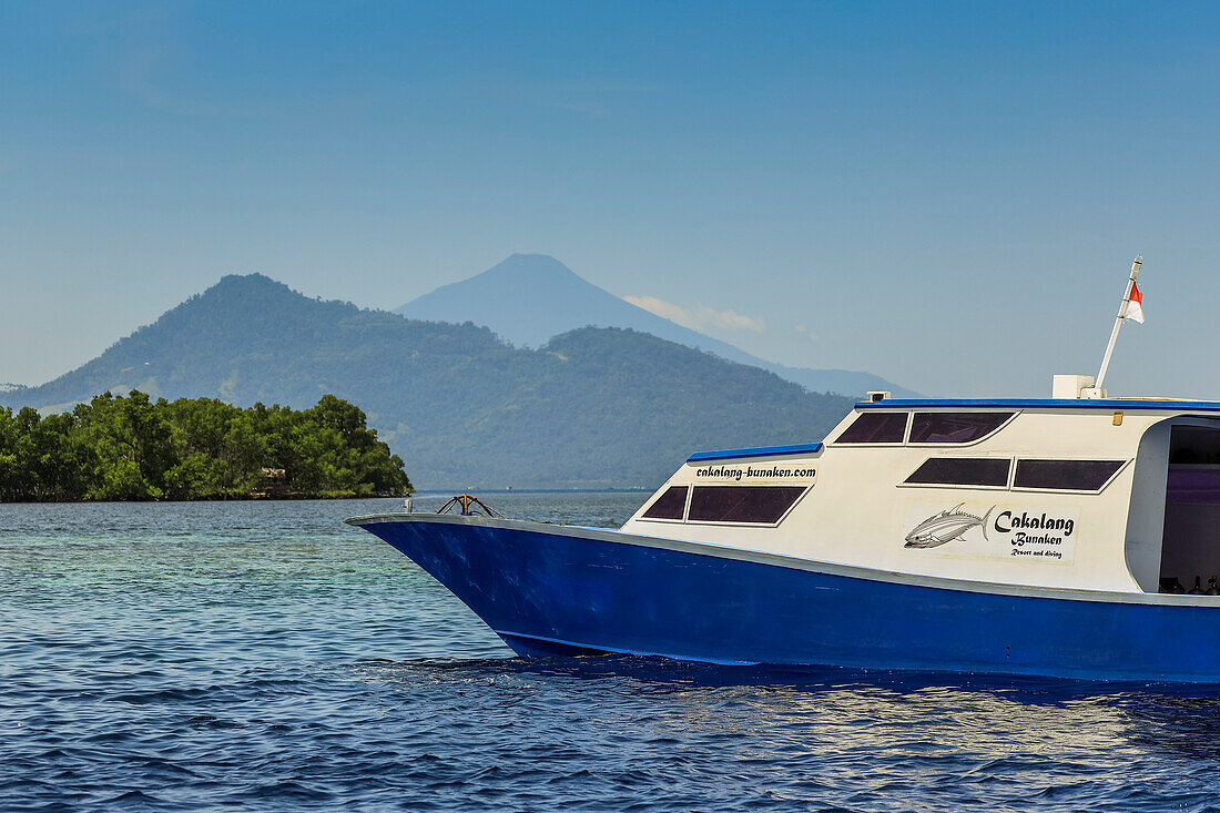 Dive boat with mainland and Manadotua Island beyond, off this coral fringed holiday and scuba island, Bunaken, North Sulawesi, Indonesia, Southeast Asia, Asia