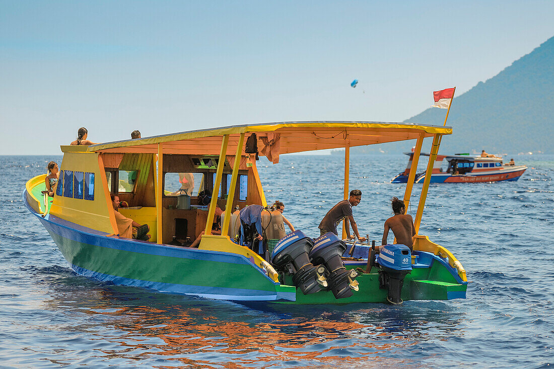 Tauchboot mit jungen ausländischen Touristen und Besatzung vor der von Korallen gesäumten Urlaubs- und Tauchinsel, Bunaken, Nordsulawesi, Indonesien, Südostasien, Asien