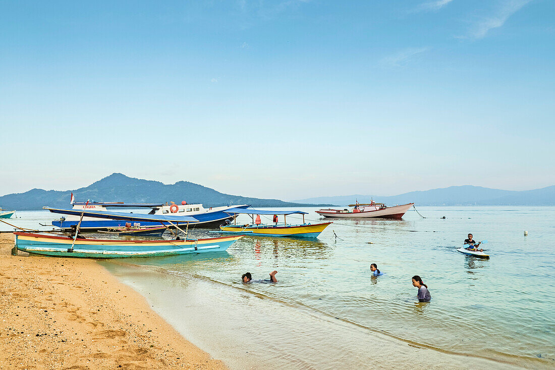 Locals swimming at the town beach with mainland beyond on this coral fringed holiday island, Bunaken Island, Sulawesi, Indonesia, Southeast Asia, Asia