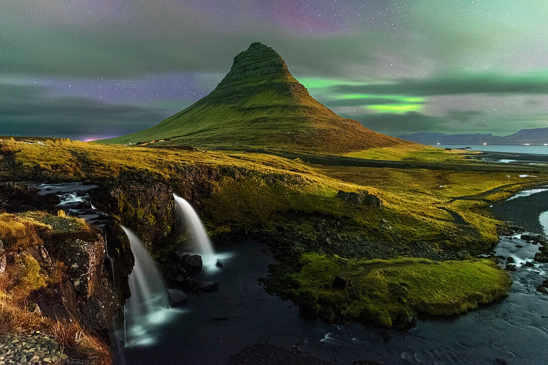Berg Kirkjufell und Wasserfall Kirkjufellfoss mit verblasstem Nordlicht (Aurora Borealis) hinter Wolken, Halbinsel Snaefellsnes, Westisland, Island, Polarregionen