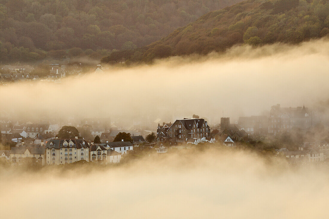 Sea fog envelops the coastal town of Lynton, lit by the light of sunset, seen from Countisbury Hill, Exmoor National Park, Devon, England, United Kingdom, Europe