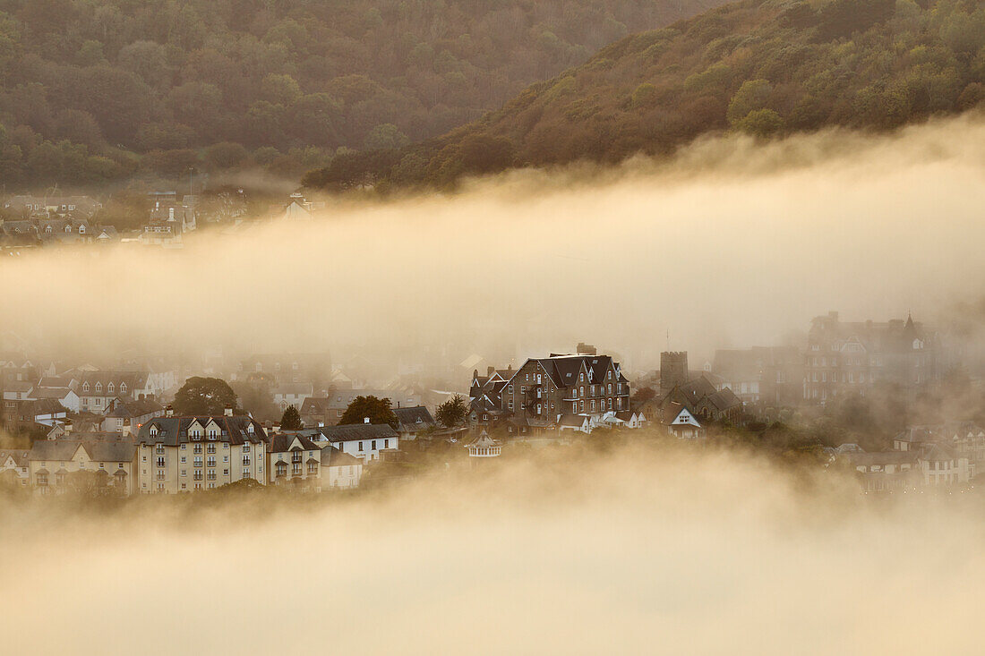 Seenebel umhüllt die Küstenstadt Lynton, beleuchtet vom Licht des Sonnenuntergangs, gesehen vom Countisbury Hill, Exmoor National Park, Devon, England, Vereinigtes Königreich, Europa