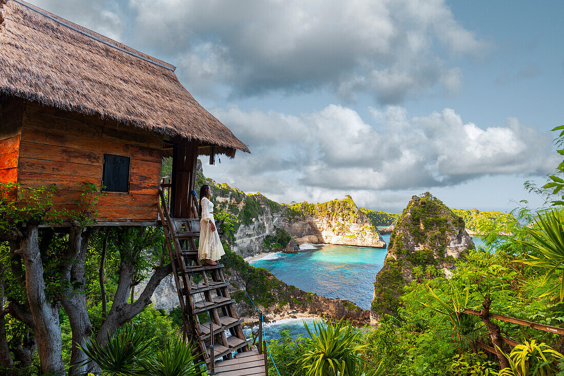 Beautiful girl with white dress standing on top of the tree house looking at the view on Diamond Beach, Nusa Penida, Klungkung regency, Bali, Indonesia, Southeast Asia, Asia