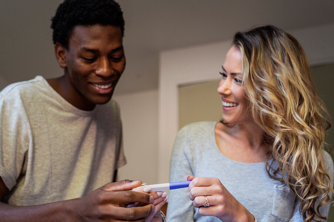 Glückliches Paar lächelt, während es einen Schwangerschaftstest im Schlafzimmer hält