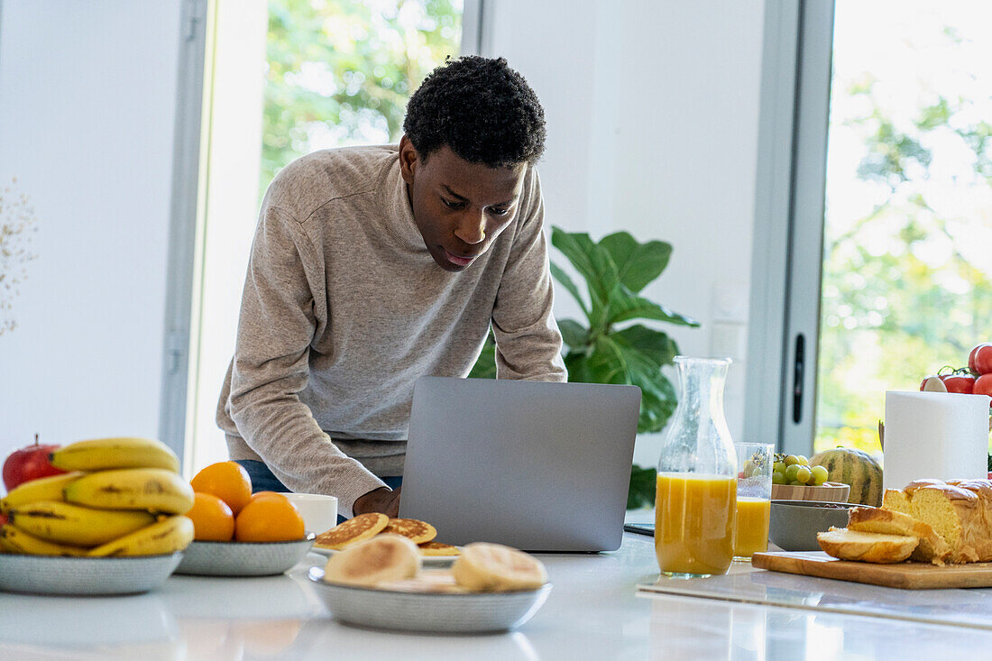 Erwachsener Mann benutzt Laptop, während er an der Küchentheke steht