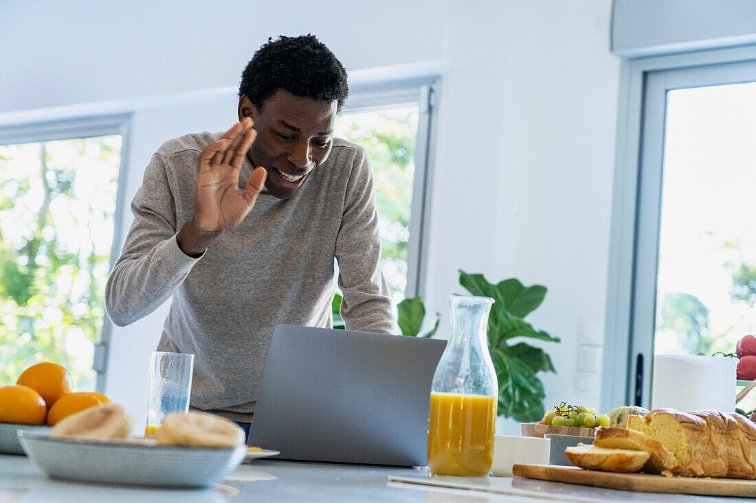 Adult man having a video call on laptop while standing at kitchen counter