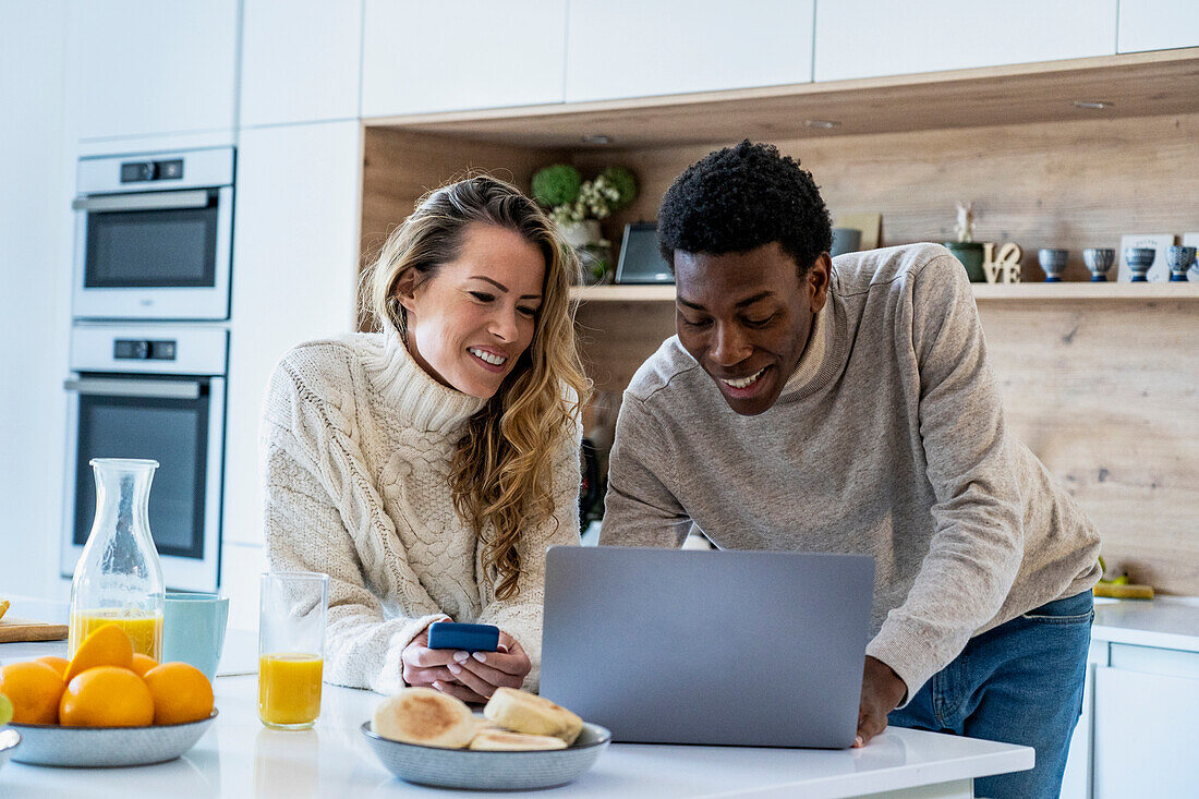 Fröhliches erwachsenes Paar, das gemeinsam einen Laptop an der Küchentheke benutzt