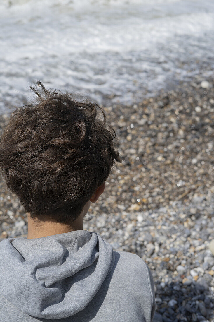Rückansicht des Kopfes einer jungen Person mit Blick auf die Wellen am Meer in der Normandie
