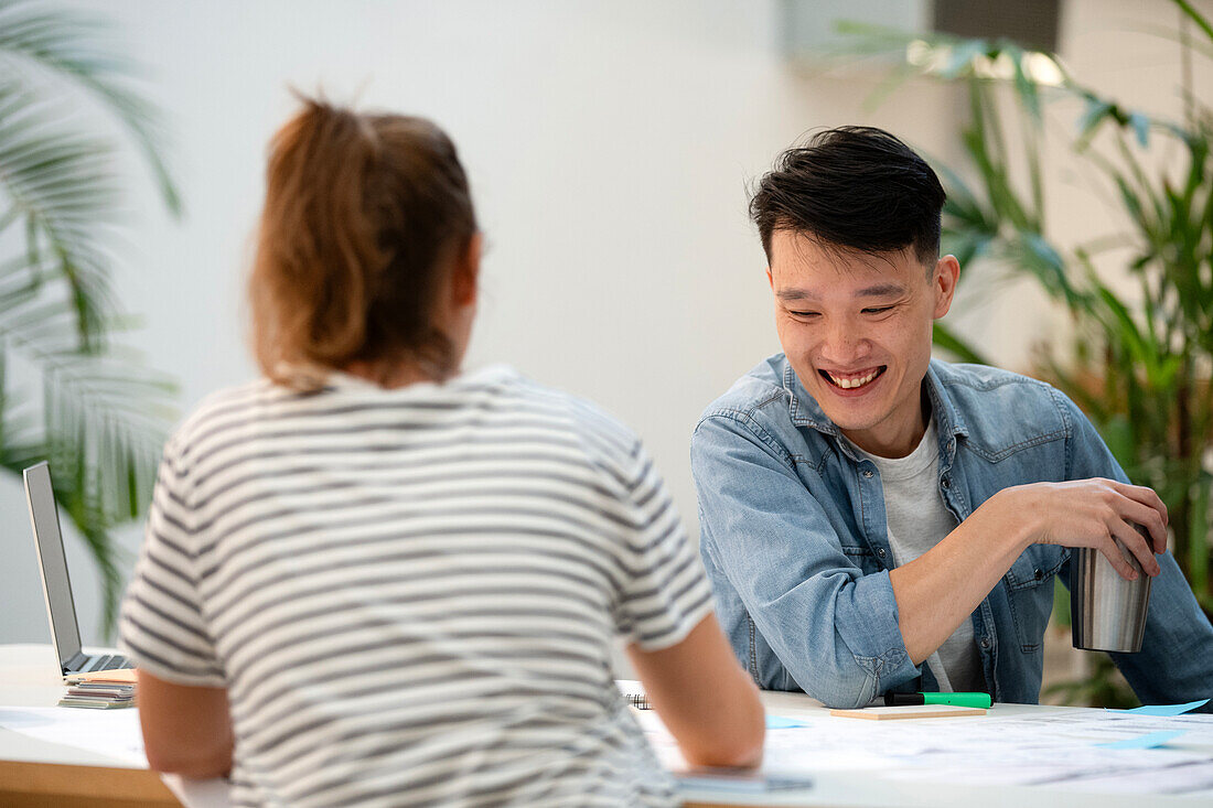 Fröhlicher junger Erwachsener, der mit einem Kollegen über Papierarbeiten diskutiert