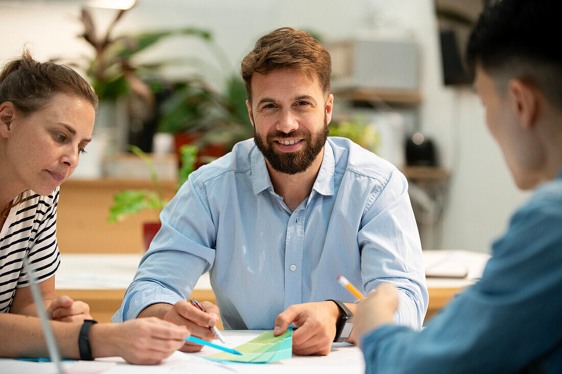 Erwachsener Geschäftsmann, der in die Kamera schaut, während er am Tisch sitzt