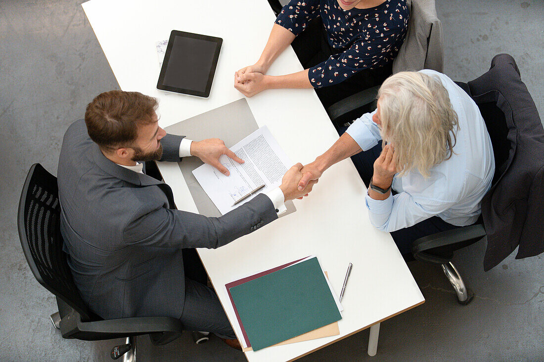 Adult couple shaking hands with lawyer after signing contract