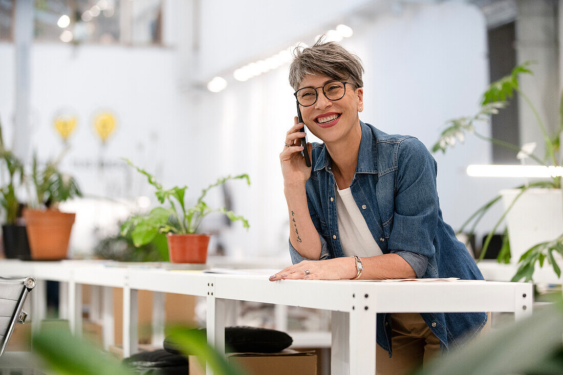 Designerin hört Voicemail ab, während sie sich auf einen Tisch stützt