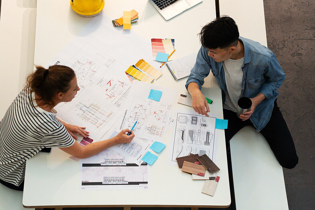 High angle view of civil engineers discussing over blueprints