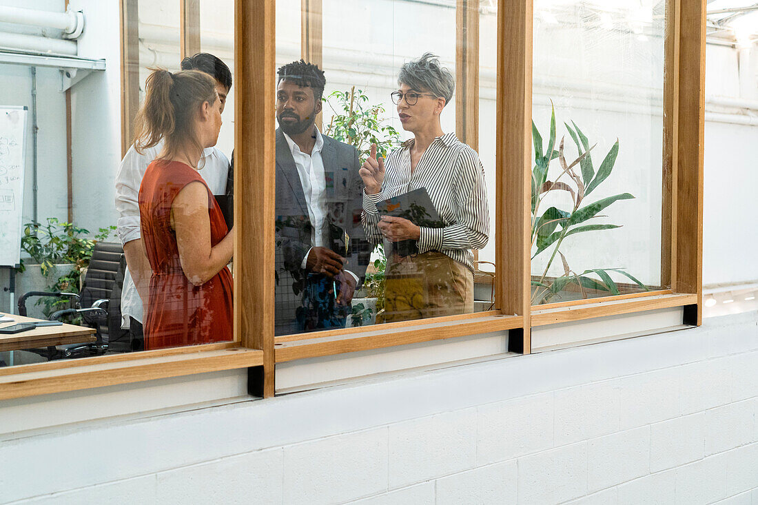 Geschäftsleute und Geschäftsfrauen diskutieren, während sie hinter dem Fenster stehen