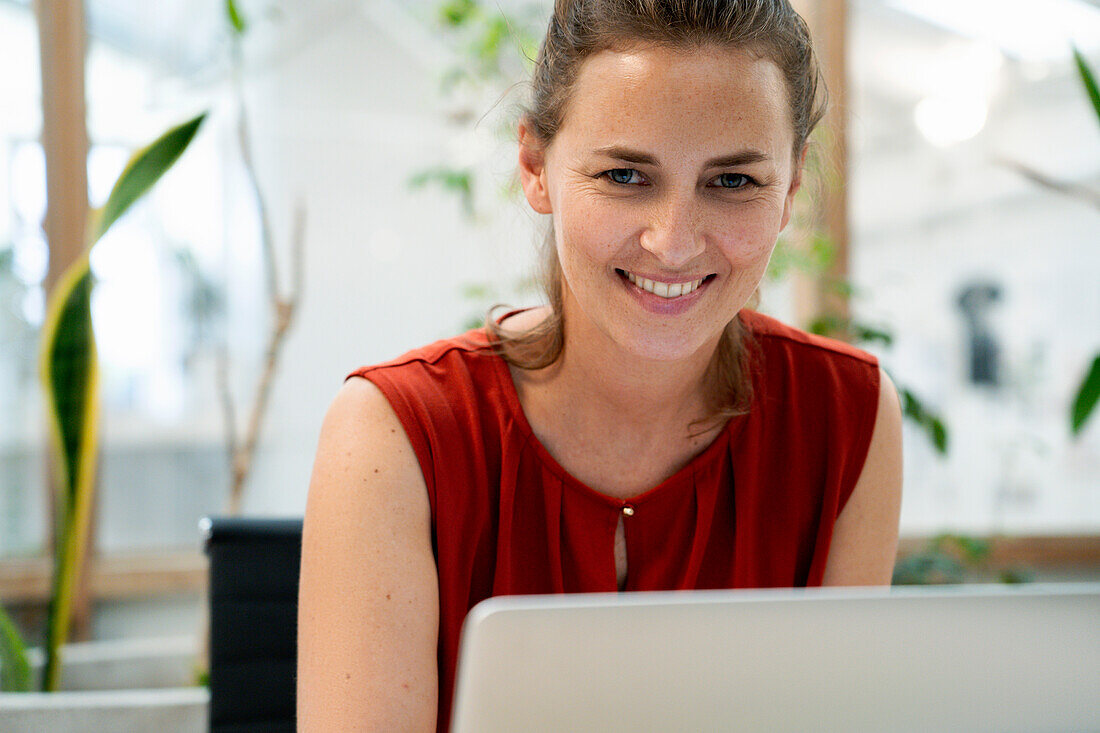 Businesswoman looking at the camera while using laptop at office