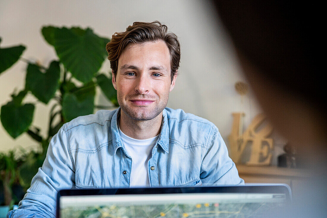 Male graphic designer looking at the camera while sitting at desk using laptop