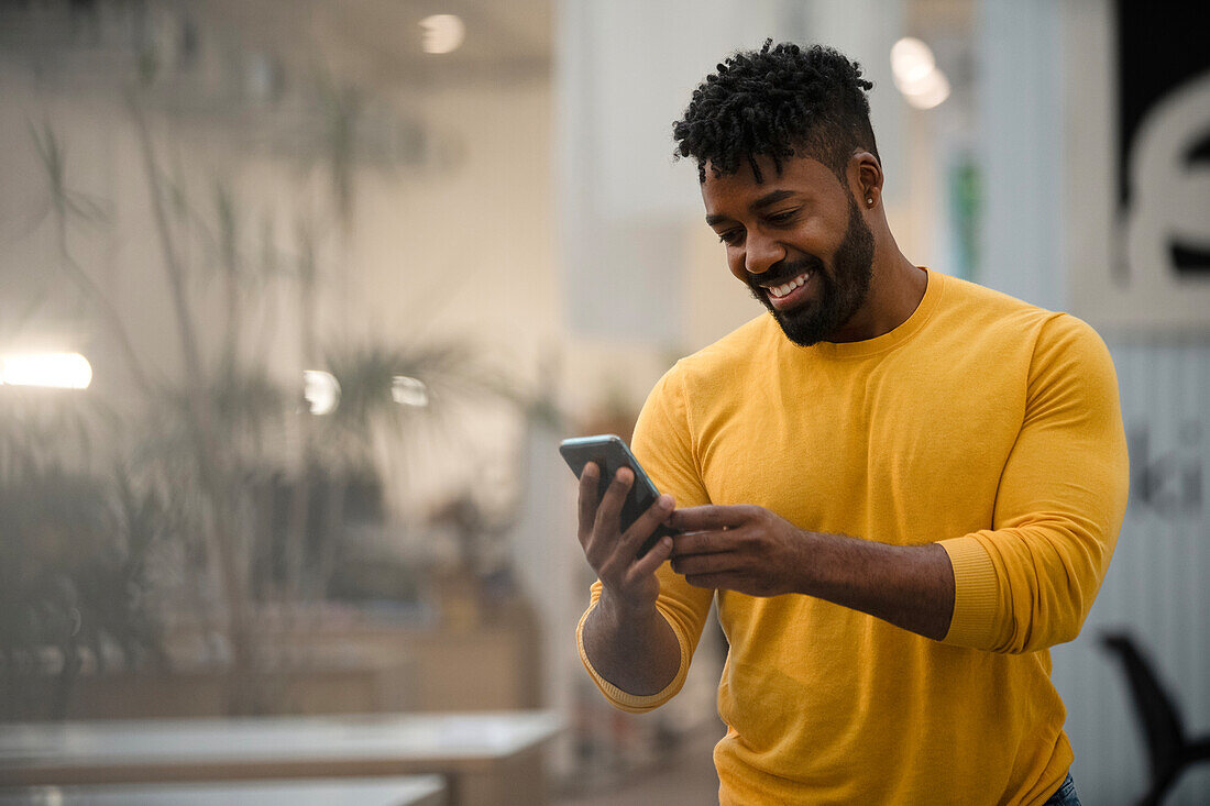 Afroamerikanischer Mann benutzt ein Smartphone, während er sich auf einen Tisch stützt